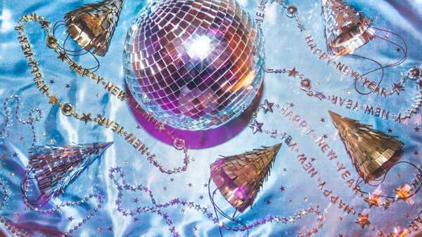 New Years party background, New Years Eve background with party favors that include a disco ball, party hats, glittering star confetti, and novelty beaded necklaces. Fun party conceptual image for New Year celebration, time, or New Years no people. Flat lay image of party supplies on winter blue background.