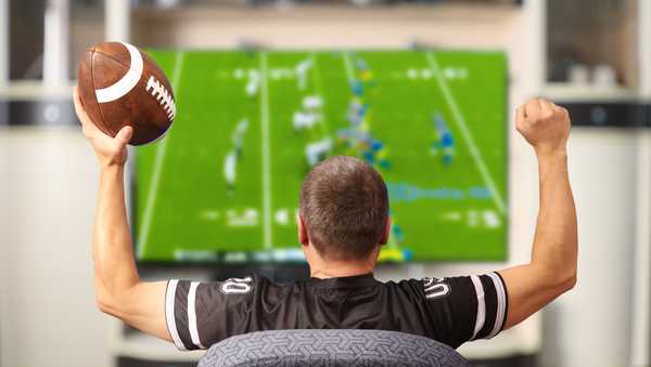 Fan of american football. Man with a ball watching TV.