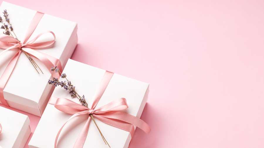 Closeup of white gift boxes tied pink ribbon with lavender decorating on pink background. Banner for Mother&apos;s day.