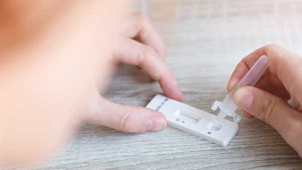 Close up of woman placing liquid drops into antigen test strip