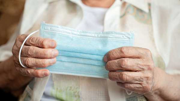 The old woman holds a medical mask in hands, preparing to wear it to protect herself from Coronavirus on quarantine