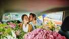Medium shot man kissing girlfriend on cheek in taxi filled with flowers