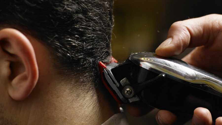 A man receives a haircut with a trimmer shown close-up.