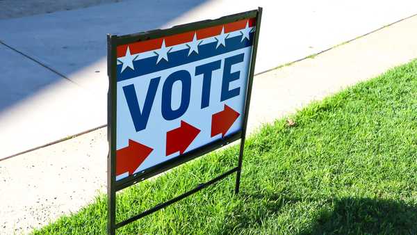 A red, white and blue sign directs citizens to the location for voting. The sign includes red directional arrows; and stars and stripes.