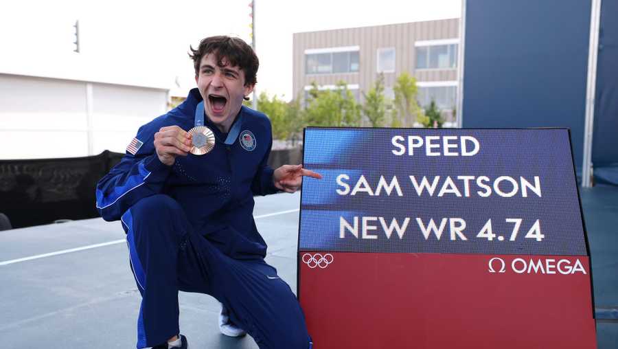 Bronze medalist Sam Watson of Team United States poses alongside a screen with his world record time of "4.74" during the Sport Climbing medal ceremony