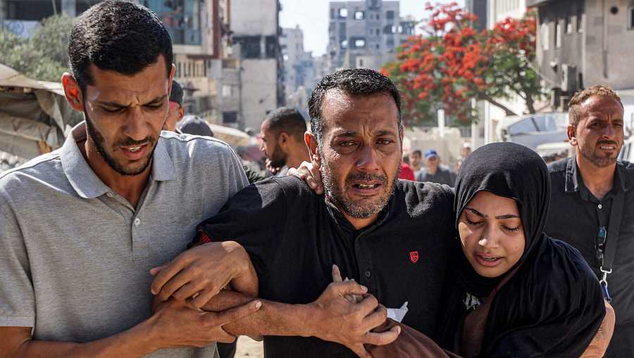 A man and woman assist another man mourning a fallen loved one during the funeral near Al-Shifa hospital in Gaza City on June 14, 2025 following reported Israeli attacks on aid queues in the Sudaniya area in northwestern Gaza.