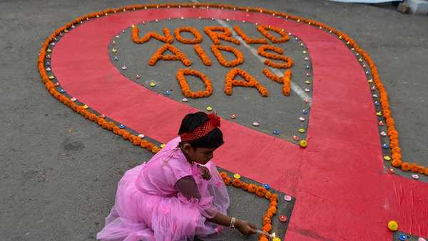 A little kid lights candles on a giant AIDS symbol as part of an awareness demonstration on World AIDS Day in Kolkata, India, on December 1, 2025 (Photo by Debarchan Chatterjee/NurPhoto via Getty Images).