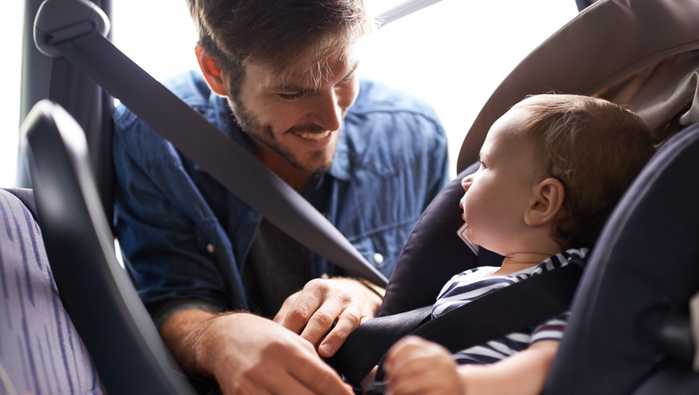 A young father strapping his baby into a car seat
