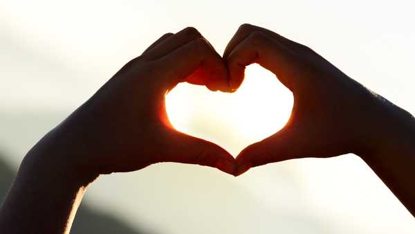 Hands forming a heart shape at sunset with mountains background.