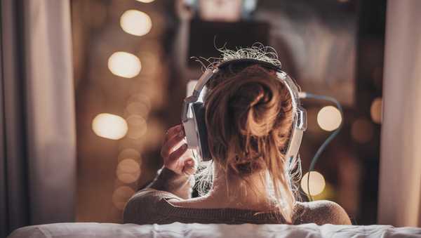 Woman using tablet pc in evening wearing big headphones, sitting in front of a big window.