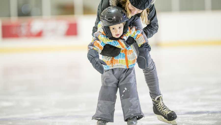 A mother is teaching her son how to ice skate at an indoor skating rink.