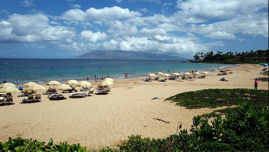 Wailea beach on a sunny day, with tourists sheltering under beach umbrellas, snorkeling, and using stand up paddleboards, Puu Kukui mountain visible in the background, Wailea, Maui, Hawaii, 2016. (Photo by Smith Collection/Gado/Getty Images).