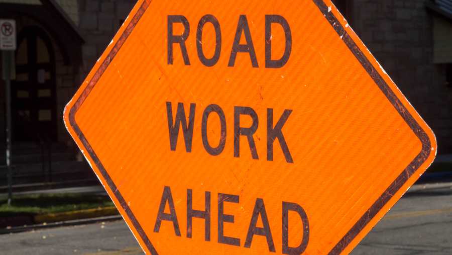 An orange diamond shaped traffic sign that says Road Work Ahead.