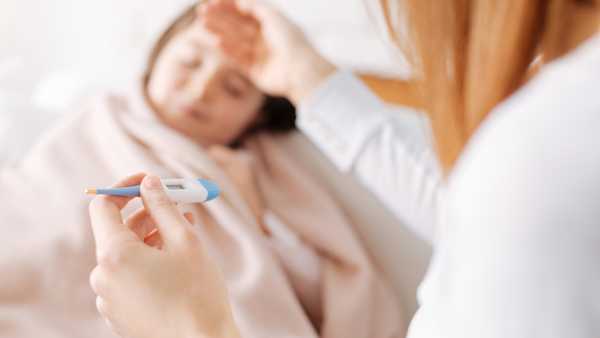 My poor girl. Caring mother holding thermometer and taking care of her sick daughter while sitting at home