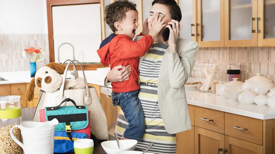 Mother holding crying son while talking on cell phone.