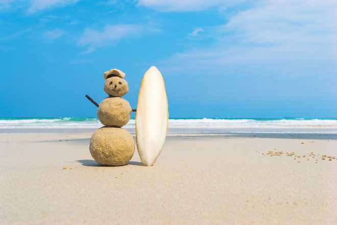Sandman with blue sea background. Handmade yellow sand surfer holding a white surf Board on a clean beach of an exotic island. the concept of entertainment and sea travel. Vacation at sea.