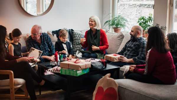 boy showing christmas presents to multi-generation family at living room