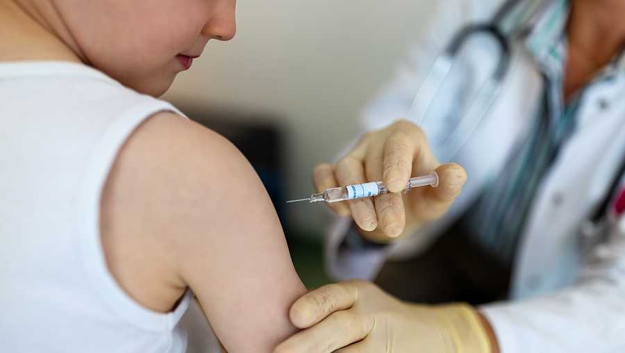 Boy getting a flu vaccine in the clinic. Small boy getting a vaccine on his arm by a pediatrician wearing gloves.