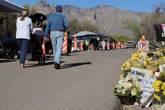 Neighbors walk by a growing memorial for Nancy Guthrie, the missing mother of "Today" show host Savannah Guthrie, outside her home in Tucson, Ariz., Sunday, Feb. 22, 2026.