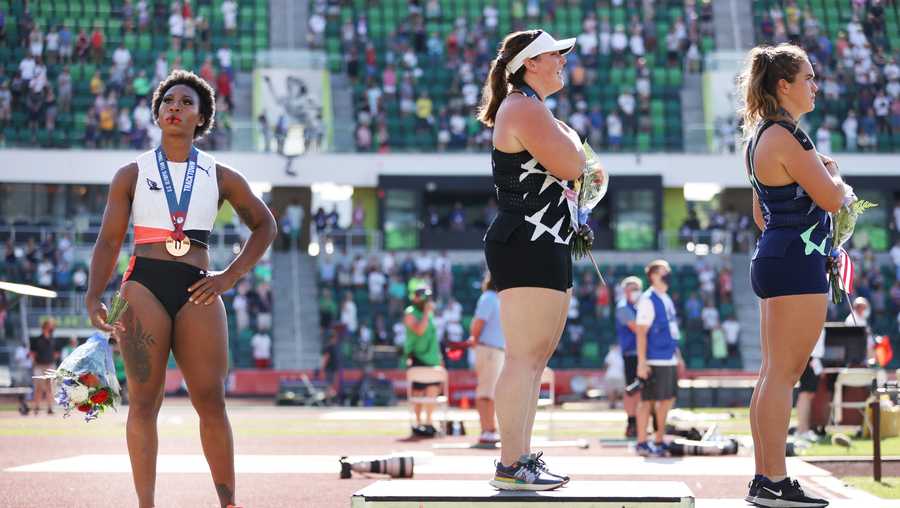 Gwendolyn Berry (L), third place, looks on during the playing of the national anthem with DeAnna Price (C), first place, and Brooke Andersen, second place, on the podium after the Women's Hammer Throw final on day nine of the 2020 U.S. Olympic Track & Field Team Trials at Hayward Field on June 26, 2021 in Eugene, Oregon.