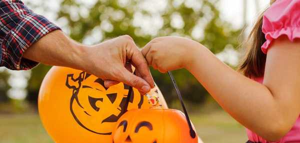 Little kid trick-or-treating on Halloween. man's hand puts a candy in the basket