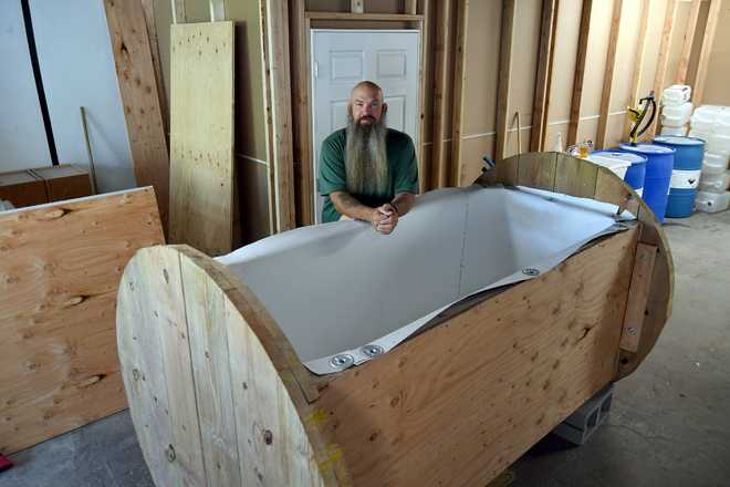 In&#x20;this&#x20;Wednesday,&#x20;Aug.&#x20;11,&#x20;2021,&#x20;photo,&#x20;Seth&#x20;Viddal,&#x20;who&#x20;co-owns&#x20;The&#x20;Natural&#x20;Funeral,&#x20;stands&#x20;behind&#x20;a&#x20;nearly&#x20;completed&#x20;human&#x20;body&#x20;composting&#x20;vessel&#x20;in&#x20;Arvada,&#x20;Colo.&#x20;On&#x20;Sept.&#x20;7,&#x20;Colorado&#x20;became&#x20;the&#x20;second&#x20;state&#x20;after&#x20;Washington&#x20;to&#x20;allow&#x20;human&#x20;body&#x20;composting,&#x20;and&#x20;Oregon&#x20;will&#x20;allow&#x20;the&#x20;practice&#x20;beginning&#x20;next&#x20;July.&#x20;The&#x20;vessel&#x20;will&#x20;be&#x20;packed&#x20;with&#x20;wood&#x20;chips&#x20;and&#x20;straw&#x20;and&#x20;will&#x20;be&#x20;able&#x20;to&#x20;compost&#x20;a&#x20;body&#x20;in&#x20;six&#x20;months.&#x20;About&#x20;the&#x20;size&#x20;of&#x20;a&#x20;standard&#x20;grave,&#x20;the&#x20;rectangular&#x20;insulated&#x20;wooden&#x20;box&#x20;is&#x20;lined&#x20;with&#x20;waterproof&#x20;roofing&#x20;material&#x20;and&#x20;packed&#x20;with&#x20;wood&#x20;chips&#x20;and&#x20;straw.&#x20;Two&#x20;large&#x20;spool&#x20;wheels&#x20;on&#x20;either&#x20;end&#x20;allow&#x20;it&#x20;to&#x20;be&#x20;rolled&#x20;across&#x20;the&#x20;floor,&#x20;providing&#x20;the&#x20;oxygenation,&#x20;agitation&#x20;and&#x20;absorption&#x20;required&#x20;for&#x20;a&#x20;body&#x20;to&#x20;compost.