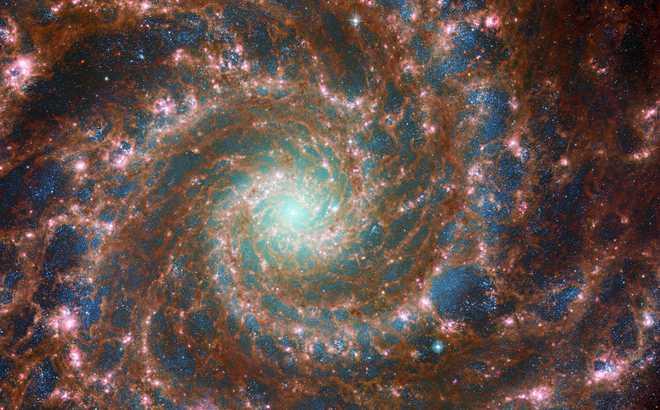 M74 shines at its brightest in this combined optical/mid-infrared image, featuring  x20;data from both the NASA/ESA Hubble Space Telescope and the NASA/ ESA/CSA James Webb Space Telescope. The dust threaded through the arms  of the galaxy is coloured red, and the young stars throughout the  arms and the nuclear core are picked out in blue, by the  James Webb Space Telescope’s Mid-InfraRed Instrument – MIRI. Meanwhile,  the Hubble Space Telescope’s Advanced Camera for Surveys adds depth: the  x20;glow of the heavier, older stars towards the gal  axy’s centre are primarily yellow, combined with the blue in this  image to make a spooky green glow. The red bubbles of star  formation are also visible in Hubble’s optical wavelengths. Scientists combine data  from telescopes operating across the electromagnetic spectrum to truly understand astronomical objects.  In this way, data from Hubble and Webb compliment each other to  provide a comprehensive view of the spectacular M74 galaxy. Links  Image  A Image C