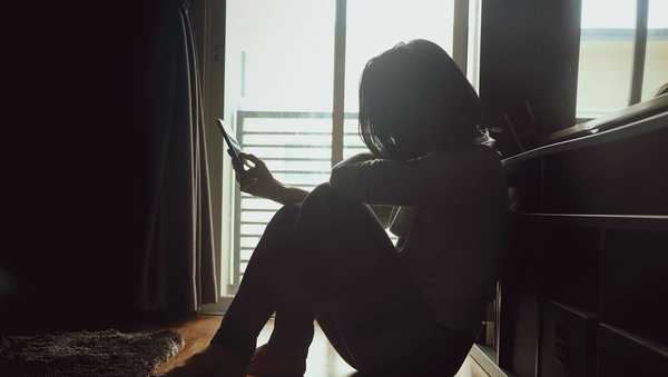 Asian women with short and black hair in casual wear, sitting on a wooden floor side the window with some light in dark tone room and holding a mobile phone. Maybe she's cheating something to somebody