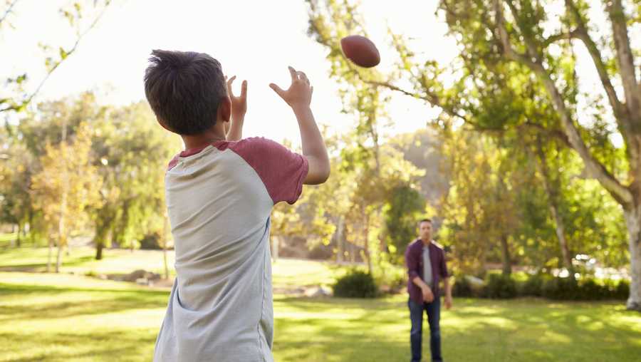 Dad and son throwing football to each other in park