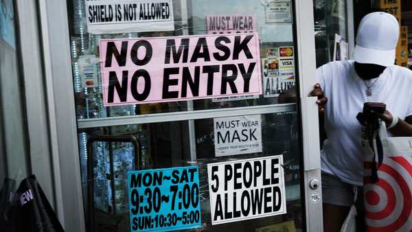 NEW YORK CITY - JULY 26: People walk out of a store requesting that people wear masks on July 26, 2021 in the Brooklyn borough of New York City. Due to the rapidly spreading Delta variant, New York City Mayor Bill de Blasio has announced that the city will require all city workers to be vaccinated or tested weekly for COVID-19. Currently, about 54 percent of New Yorkers have taken the vaccine. (Photo by Spencer Platt/Getty Images)