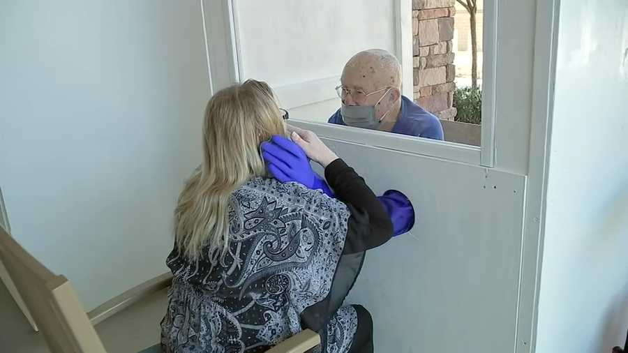 A resident of a Texas assisted living facility embraces a loved one using the "hug booth."