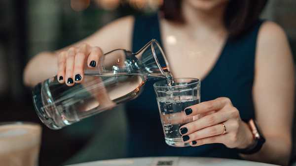 woman pouring water from a water bottle, keeping hydrated during summer.