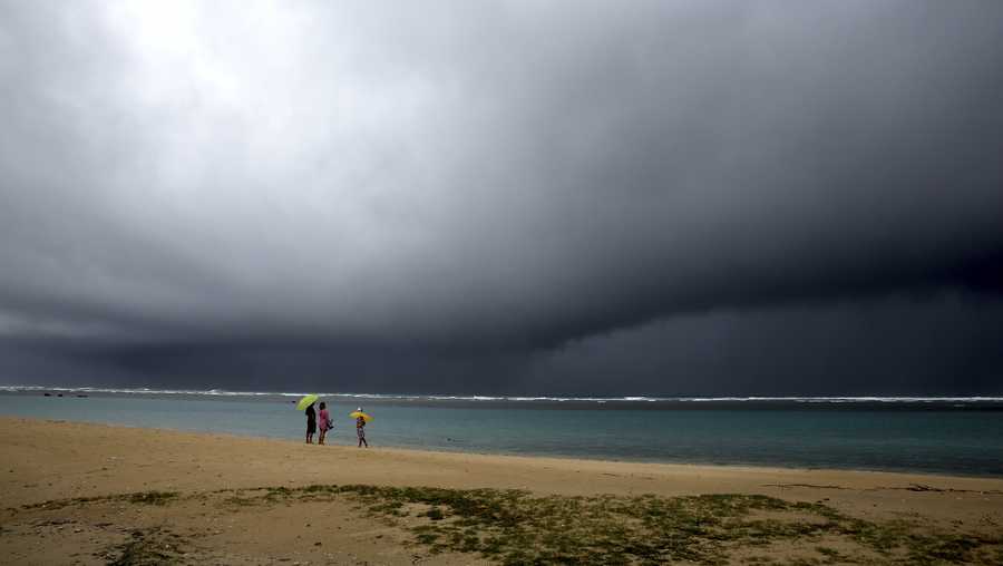 People hold umbrellas as it begins to rain on an otherwise empty beach in Honolulu on Dec. 6.