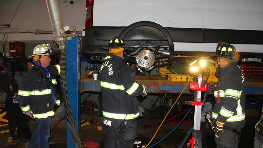 Firefighters work to free mechanic caught under vehicle lift.