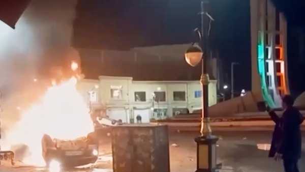 This frame grab from a video released Friday, Jan. 9, 2026, by Iranian state television shows a man holding a device to document burning vehicles during a night of mass protests in Zanjan, Iran.