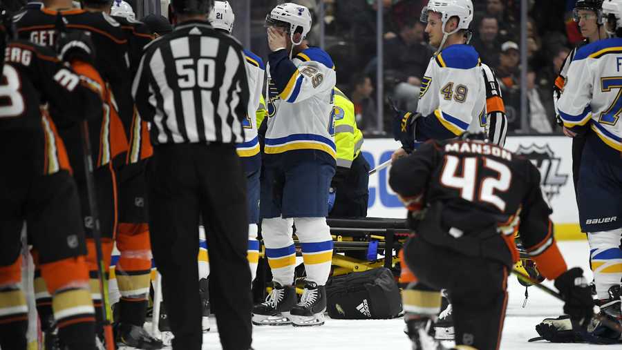 St. Louis Blues defenseman Vince Dunn, left, of center wipes his faces as Anaheim Ducks defenseman Josh Manson kneels on the ice while blues defenseman Jay Bouwmeester, who suffered a medical emergency, is worked on by medical personnel during the first period of an NHL hockey game Tuesday, Feb. 11, 2020, in Anaheim, Calif.