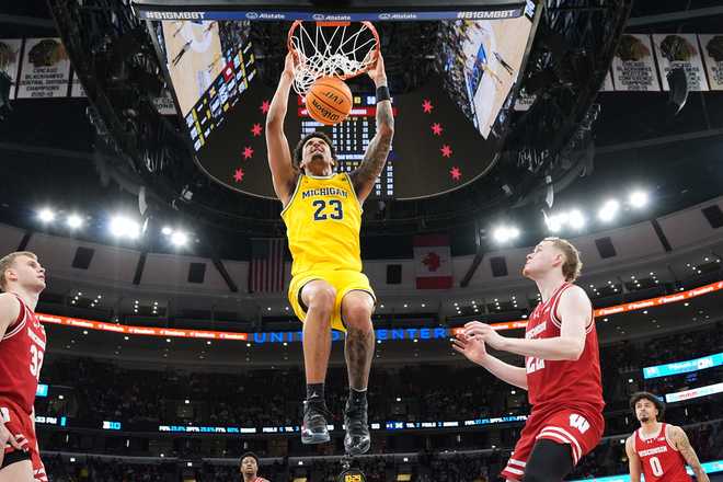 Michigan forward Yaxel Lendeborg hangs from the rim after dunking during the second half of an NCAA college basketball game against Wisconsin in the semifinals of the Big 10 Conference tournament, Saturday, March 14, 2026, in Chicago.