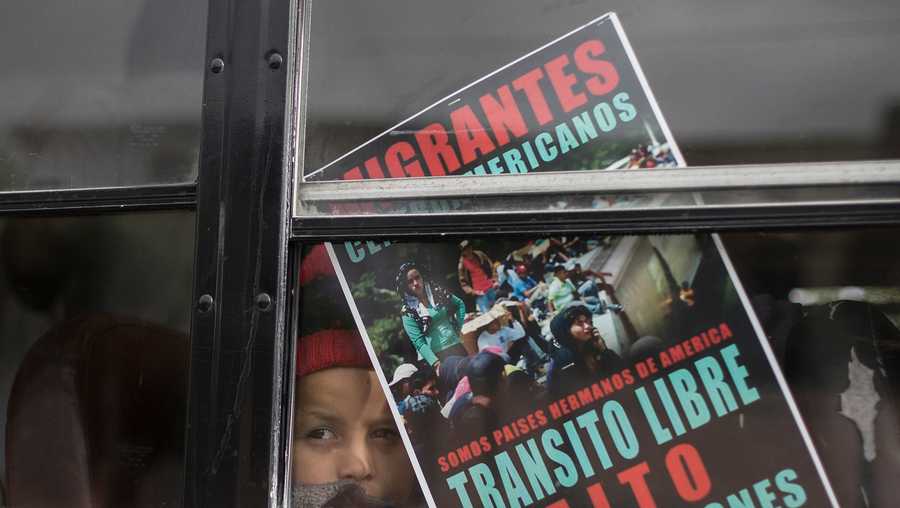 A Central American child who is traveling with a caravan of migrants, peers from a bus carrying the group to the border wall for a gathering of migrants living on both sides of the border, in Tijuana, Mexico, Sunday, April 29, 2018. The sign reads in Spanish: We're all brother countries from the Americas. Free transit. Stop the deportations."