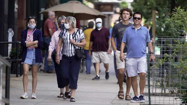 Pedestrians with and without face masks walk in downtown Omaha, Neb., Friday, July 31, 2020.