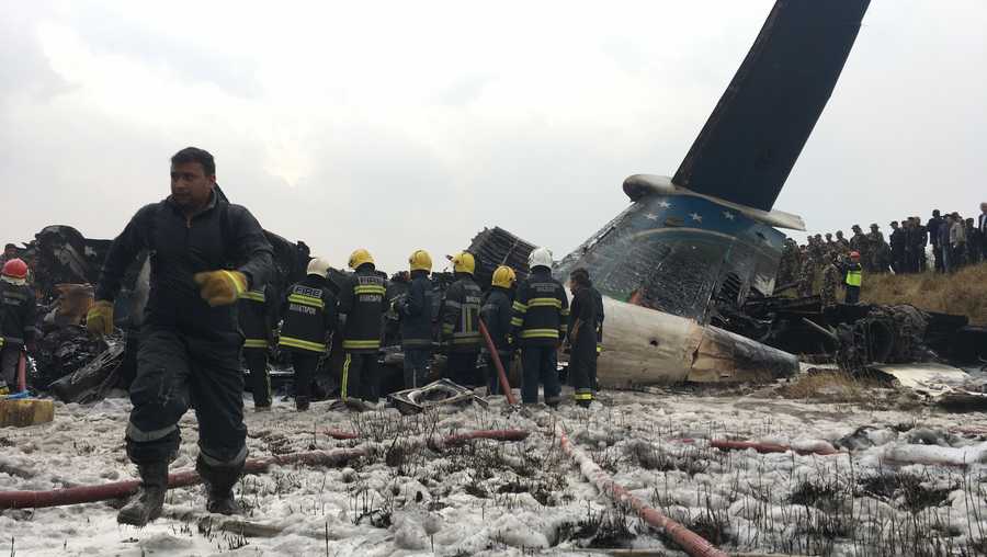 Nepalese rescuers stand near a passenger plane from Bangladesh that crashed at the airport in Kathmandu, Nepal, Monday, March 12, 2018.