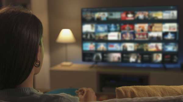 Young woman relaxing on the couch at home and watching videos on demand on her TV, entertainment concept