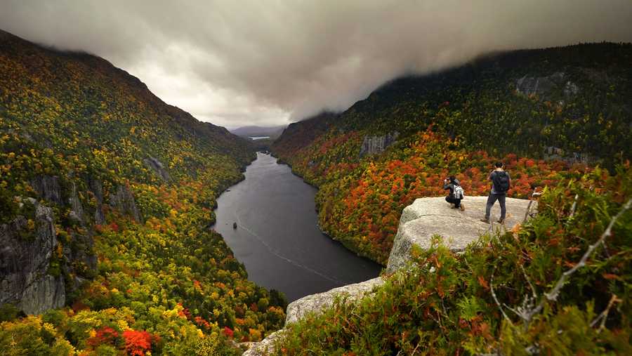 Two visitors photograph the in the colorful autumn view at the Indian Head vista overlooking Lower Ausable Lake in the Adirondacks, Sunday, Sept. 27, 2020, near Keene Valley, N.Y. (AP Photo/Robert F. Bukaty)