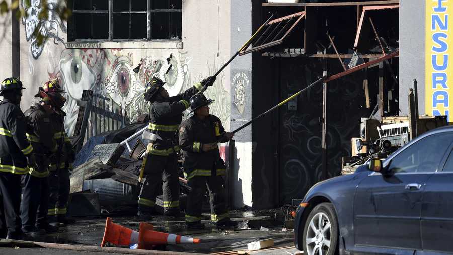 Firefighters clear an entry to a smoldering building after a fire tore through a warehouse party early Saturday.