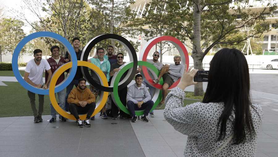 A group of students from Uruguay pose for a souvenir picture on the Olympic Rings set outside the Olympic Stadium in Tokyo, Saturday, March 21, 2020.