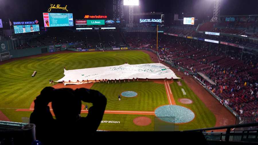 A fan watches as the grounds crew covers the infield as rain falls during the fifth inning of a baseball game between the Boston Red Sox and Tampa Bay Rays, Tuesday, Oct. 4, 2022, at Fenway Park, in Boston.