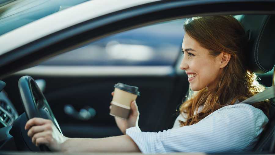 Shot of a businesswoman holding coffee to go and driving a car during her morning commute.