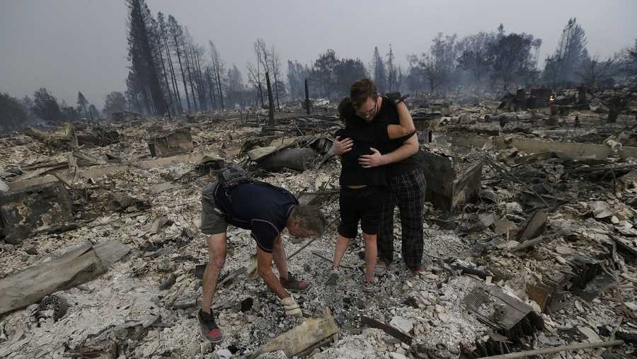 Michael Pond, left, looks through ashes as his wife Kristine, center, gets a hug from Zack Thurston, their daughter's boyfriend, while they search the remains of their home destroyed by fires in Santa Rosa.