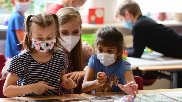 Students, wearing face masks, listen to their teacher during a summer project at school.