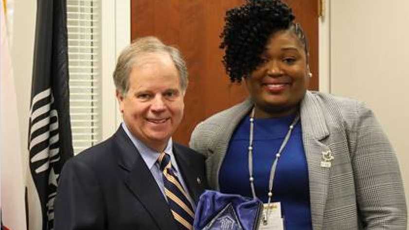 Senator Doug Jones receives the 2019 Distinguished Community Health Defender Award from the CEO of the Rural Health Medical Program Keshee Dozier-Smith