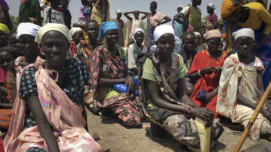 In this photo taken Wednesday, March 1, 2017, women sit in line on the ground waiting to receive food distributed by the World Food Program (WFP) in Padeah, South Sudan. South Sudanese who fled famine and fighting in Leer county emerged from South Sudan's swamps after months in hiding to receive food aid being distributed by the World Food Program.